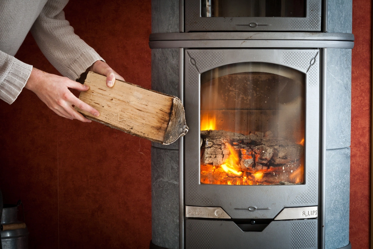 Personne ajoutant une bûche dans un poêle à bois allumé, montrant la combustion des bûches à l'intérieur.